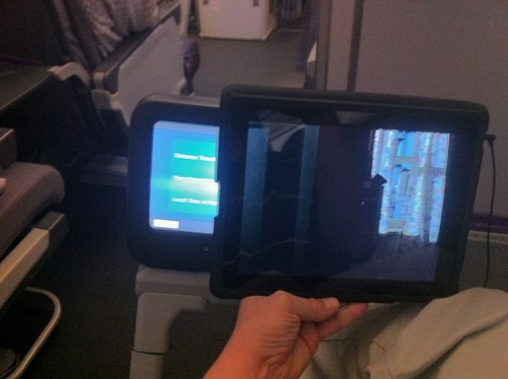 Fold the front cover of the case over backwards, but don't slot it into the retaining tab -- just let it hang free. Then slide the iPad over the inflight entertainment screen.