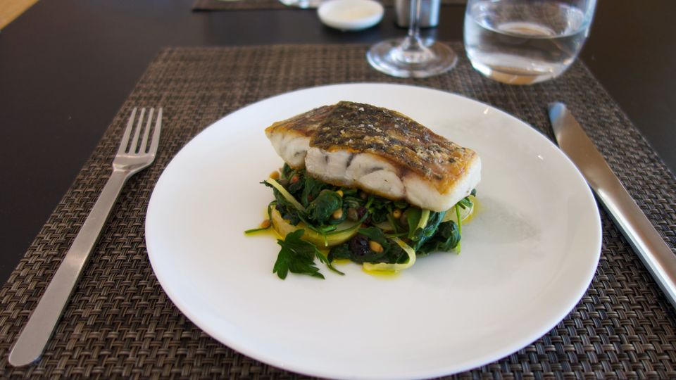 New to the Qantas First Lounge summer menu: grilled barramundi with a Sicilian-style agrodolce garnish of olives, capers, pine nuts and currants mixed with buttery spinach.